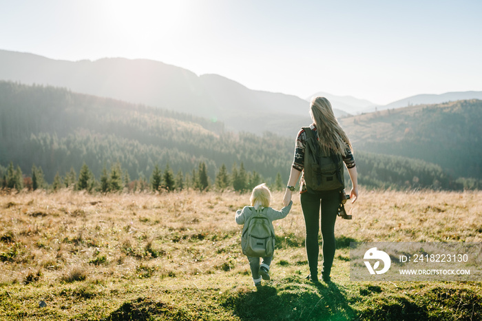 Mom with backpack and child walk in autumn grass. The daughter and mother walking on nature. Family 