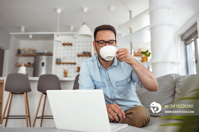 Technology, people and lifestyle concept - happy man with laptop computer drinking coffee or tea at 