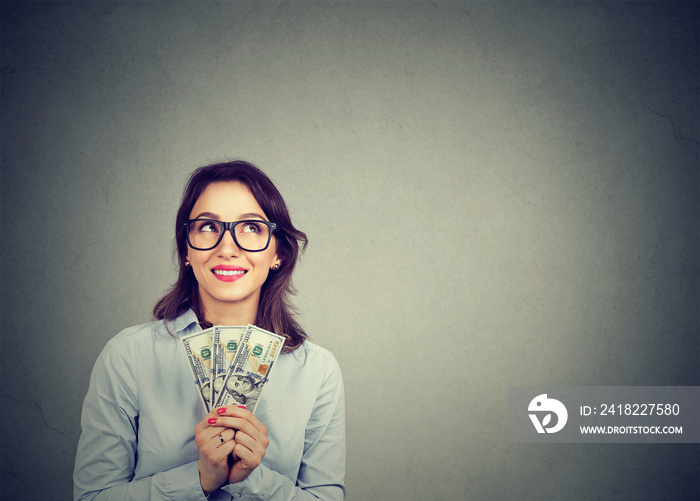 Happy daydreaming business woman with money dollar bills in hand imagining how to spend them