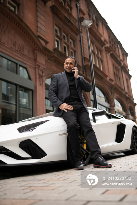 Mature man leaning against luxury car and using phone