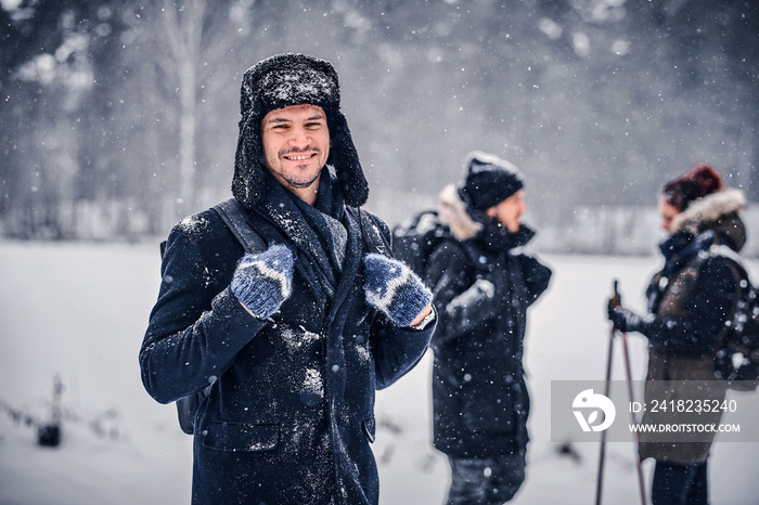 Portrait of a smiling hiker guy with a backpack walking with his friends through a winter woods