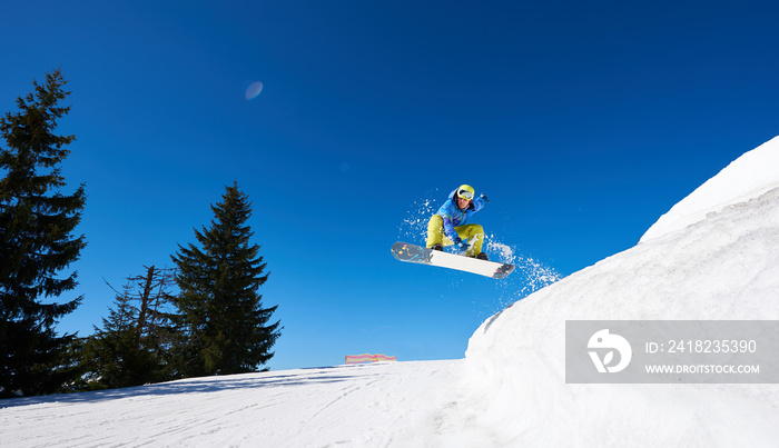 Snowboarder at jump in high mountains at sunny day against blue sky. Ski season and winter sports co