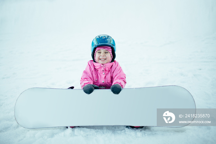 Snowboard Winter Sport. Little kid girl playing with snow wearing warm winter clothes.