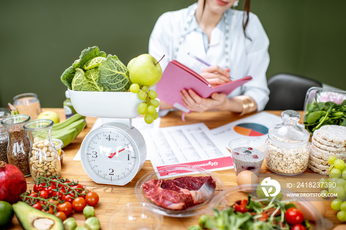 Woman dietitian working on a diet plan sitting with various healthy food ingredients, cropped image 