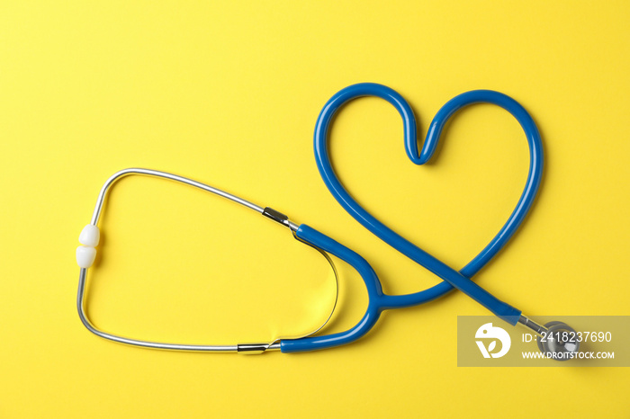 Stethoscope on yellow background, top view and space for text