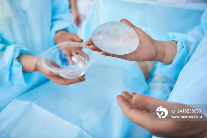 Careful doctor wearing rubber gloves while conducting plastic surgery and holding silicone implant