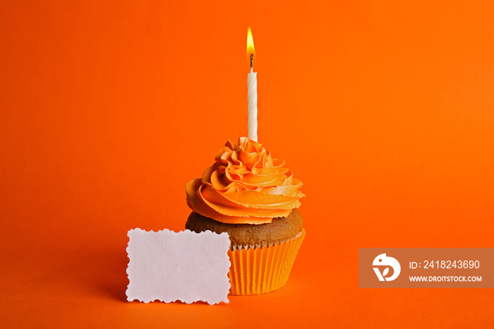 新鲜美味的纸杯蛋糕，橙色背景上有蜡烛和生日卡