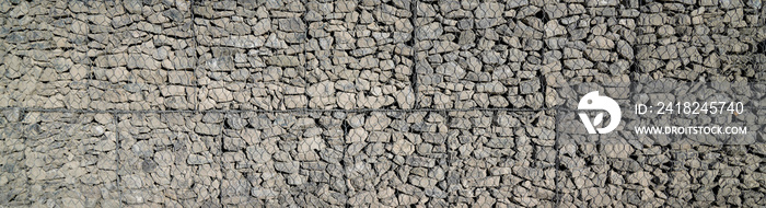 grey stone and pebbles in wire mesh wall horizontal stones facade background in panoramic web header