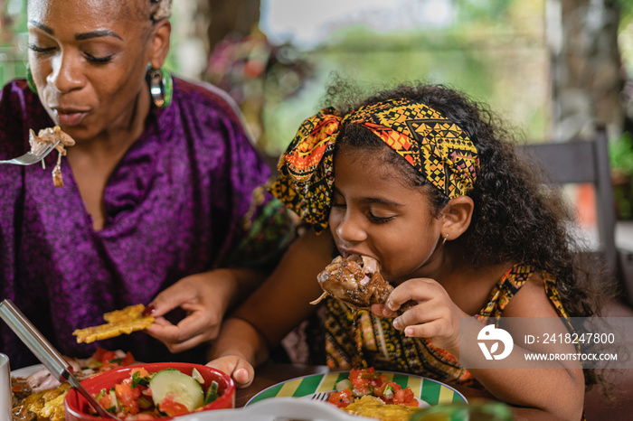 Imagen horizontal de una niña afrocaribeña disfrutando de un delicioso trozo de pollo caribeño senta