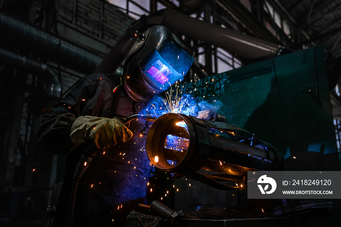 Side view of welder in protective helmet welding metal detail with sparks at factory