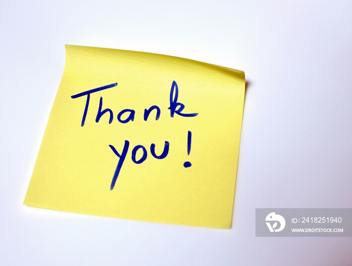 The sentence Thank you written by hand on a yellow post it and put on the white table
