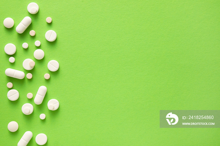 Many different pills and capsules on green background