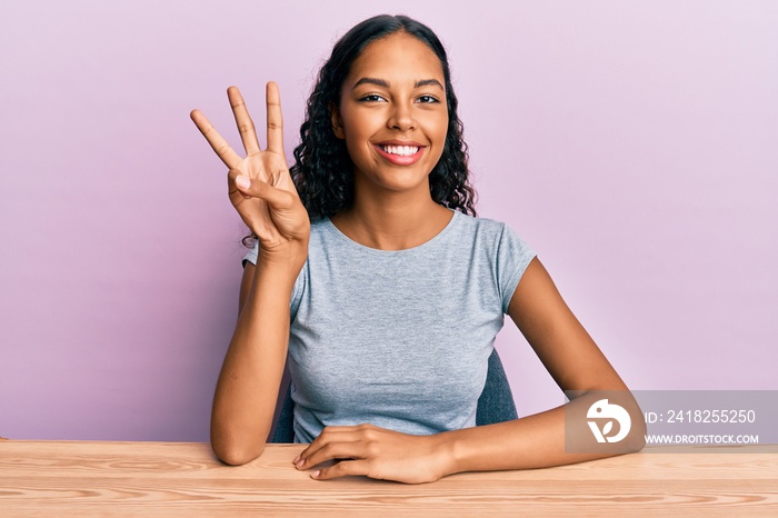 Young african american girl wearing casual clothes sitting on the table showing and pointing up with