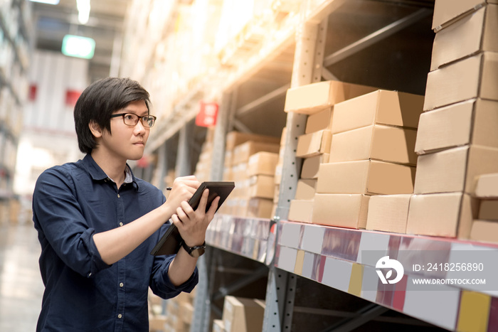 亚洲年轻人用数字在仓库货架上的纸板箱中清点产品
