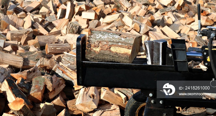 Closeup of wood splitter blade about to slice through block of firewood with split pieces piled all 