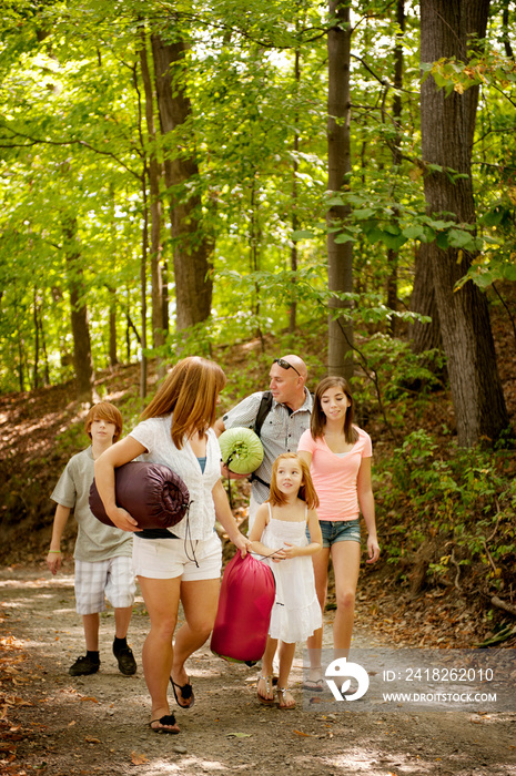 Family with three children (6-7, 12-13, 16-17) walking through woods with camping gear