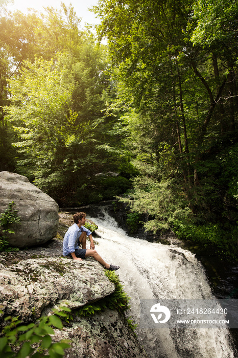 Young man looking at waterfall in forest