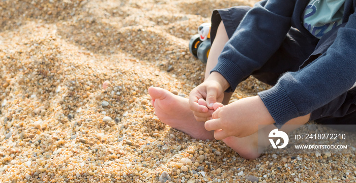 Child playing with the toes and feeling the texture of the beach sand, sensory experience