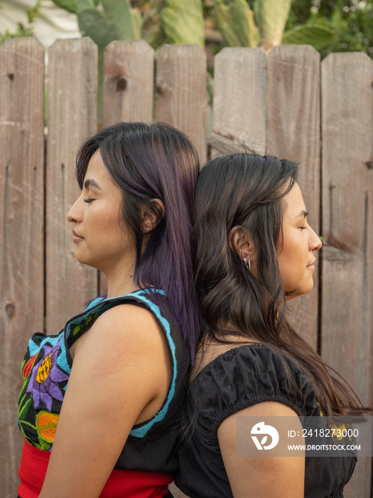 Twin sisters standing back to back with their eyes closed