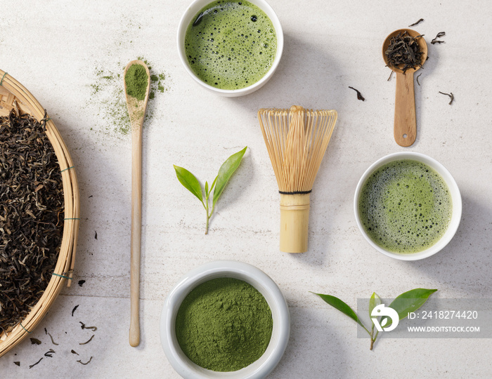 Organic matcha green tea powder in bowl with wire whisk and green tea leaf on white stone table, Org