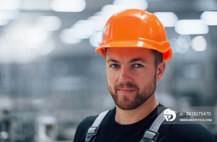 工厂室内男性工业工人的肖像。戴着橙色安全帽的年轻技术人员