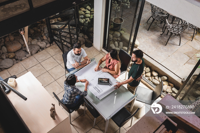 Vista superior de un Grupo de profesionales analizando planos constructivos e imágenes de un proyect