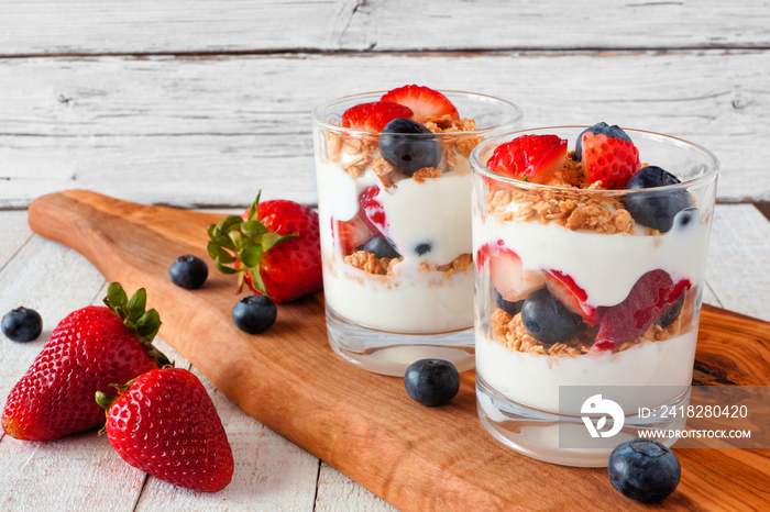 Strawberry and blueberry parfaits in glasses on a wood serving board against a white wood background