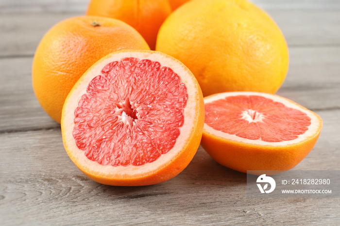 粉红色葡萄柚在木桌子上切成两半，背景是整个柑橘。