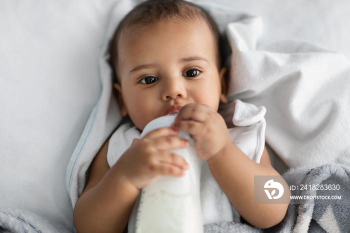 Cute little African American child drinking from baby bottle