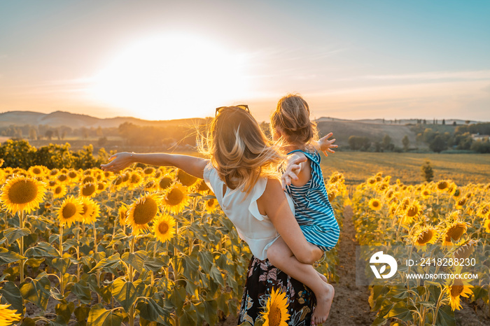 giovane mamma in braccio la figlia in campo di girasoli guardano il futuro