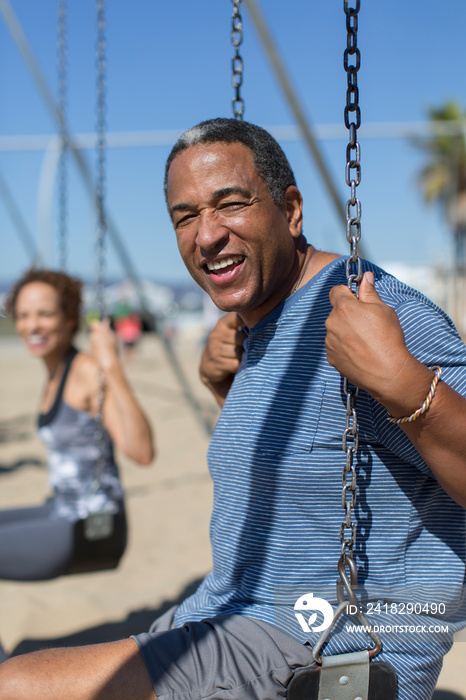 Portrait happy senior man on swing set on sunny beach