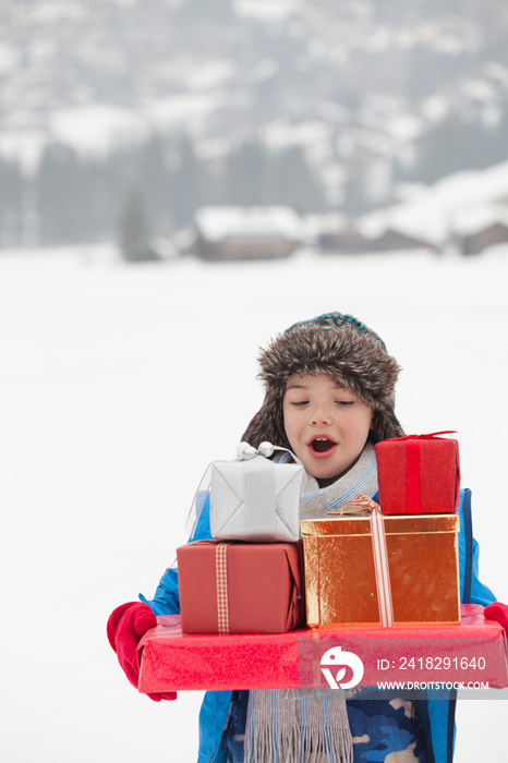 Boy carrying Christmas gifts in snowy field