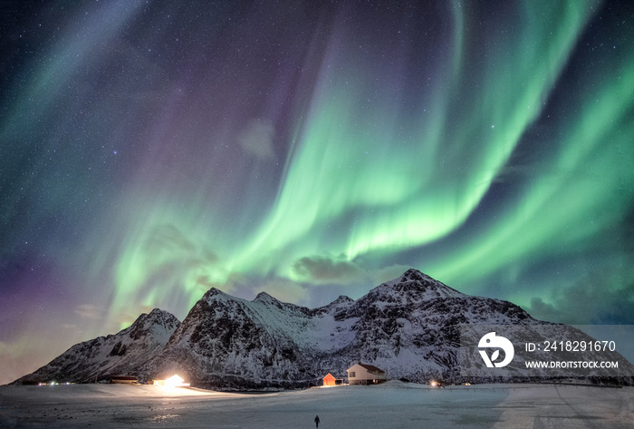 Aurora borealis with starry over snow mountain range with illumination house in Flakstad, Lofoten is