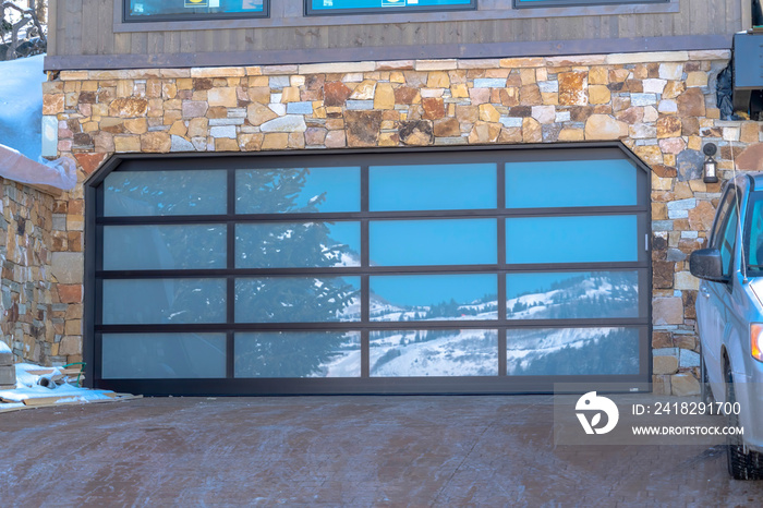 Garage door with glass panes reflecting a snowy hill landscape under blue sky