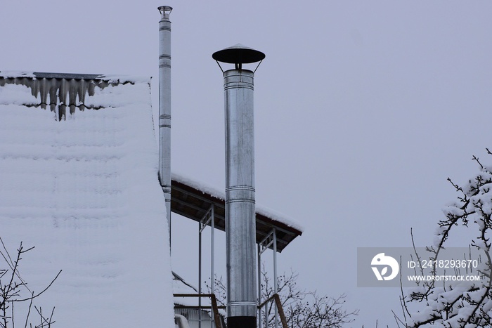 long gray metal chimney pipe on the roof in the snow against the sky