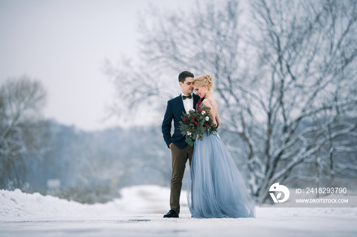 Bride and groom among snowy landscape.