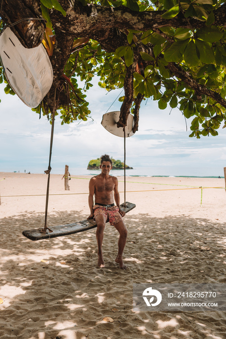 imagen de un hombre local sin camisa con cabello rizado sentado sobre un columpio en una playa del c