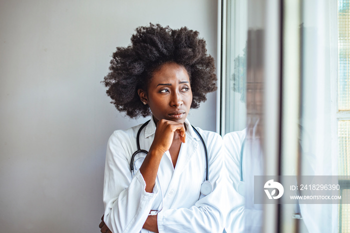 Shot of a young female doctor looking stressed out while standing at a window in a hospital. Shes b