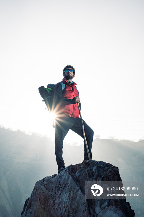 Young traveler in red snow jacket and a backpack standing on blue isolated background. Looking upwar