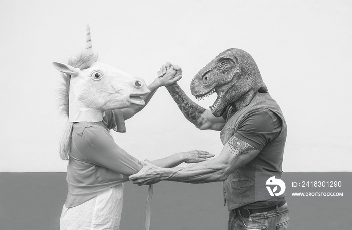 Crazy couple dancing and wearing dinosaur and unicorn mask - Senior trendy people having fun masked 