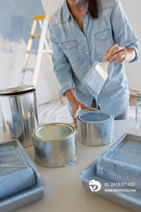 Woman dipping paintbrush into blue paint can