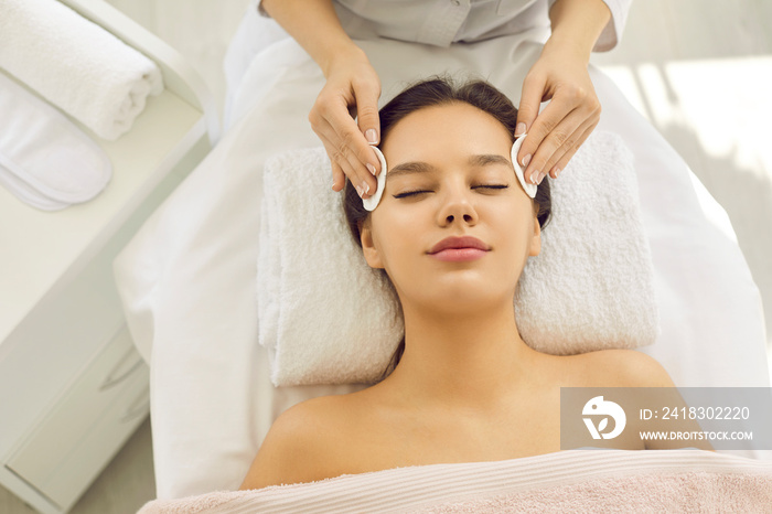 Happy beautiful woman lying on spa massage bed in beauty parlor and enjoying modern facial treatment