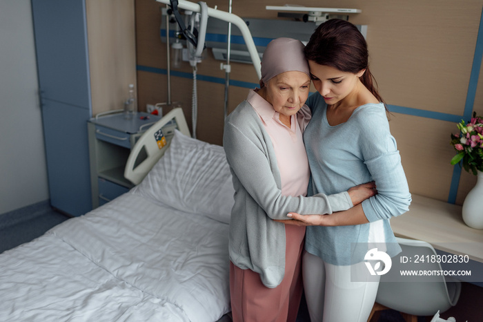 upset daughter embracing sick senior mother with cancer in hospital