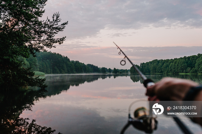 Fisherman with rod, spinning reel on the river bank. Sunrise. Fishing for pike, perch, carp. Fog aga