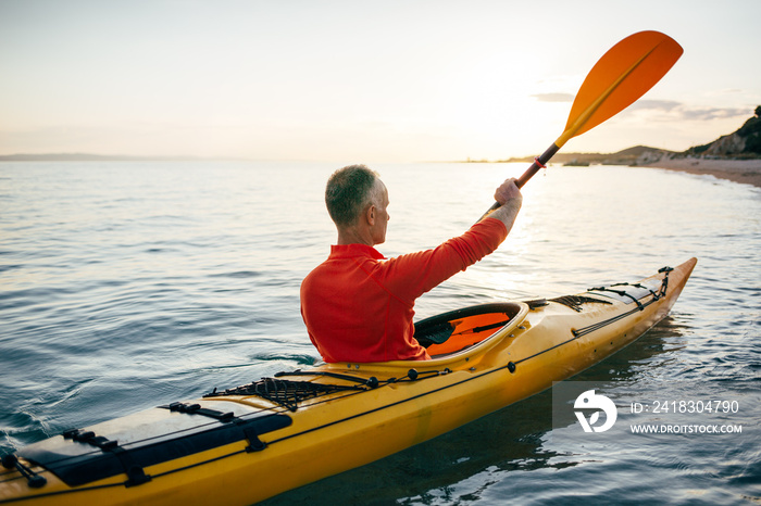 Rear view of senior man enjoy paddling kayak on the sunset sea