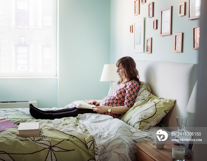 Side view of pregnant woman reading book on bed