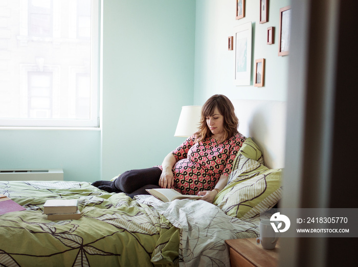 Pregnant woman reading book on bed