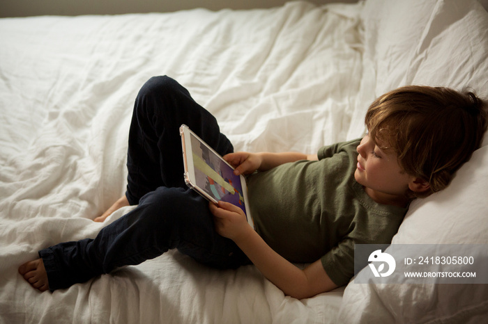 High angle view of cute boy playing games over tablet computer while lying on bed at home