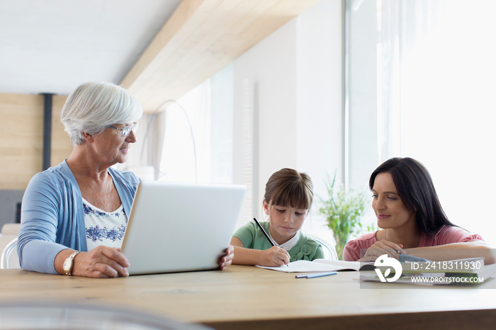 Multi-generation family using laptop and coloring at dining table