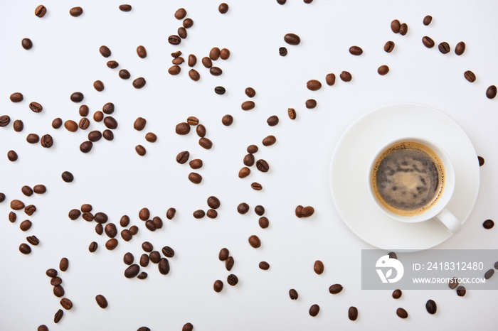 top view of delicious coffee in cup near scattered roasted beans on white background
